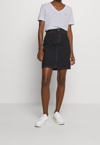 Gonna di jeans di colore blu scuro con cerniera frontale e cuciture in vista. Abbinata a una t-shirt grigia a righe con scollatura a V e scarpe da ginnastica bianche.