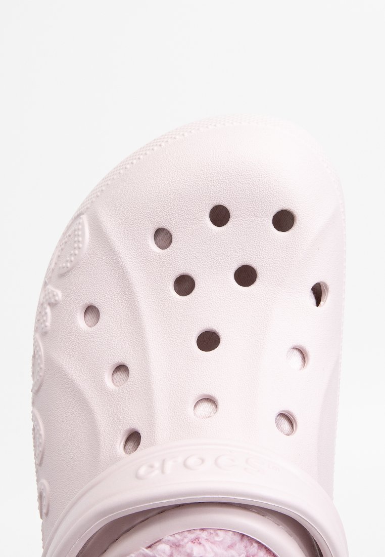 Los zuecos Crocs de color rosa claro presentan un diseño ventilado con múltiples agujeros circulares, una superficie texturizada y una plantilla acolchada.