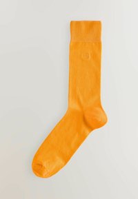 Oranžna bombažna nogavica z rebrastim robom, gladko teksturo in ojačanim prstom. Ima majhen logotip blizu roba.