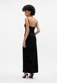 Melnas samta maxi kleita ar ziedu rakstu, plāniem siksniņām un atvērtu aizmuguri. Kojotas ar melniem augstiem papēžiem. Gluda tekstūra.