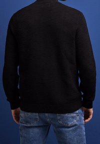 Svart stickad tröja med ribbad textur, rund hals och långa ärmar. Bärs med ljusblå jeans och har en avslappnad design.