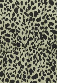Grønne stof med et sort leopardprintmønster. Designet har uregelmæssige pletter og samlinger ved taljen, hvilket skaber et tekstureret udseende.