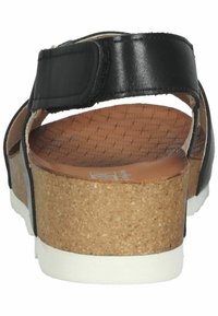 Sandalias negras con suela de cuña de corcho, con plantilla marrón texturizada y tira ajustable negra. Son visibles los acentos de cuero suave.