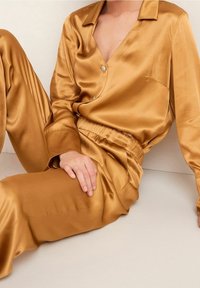 Set di pigiami in satin dorato con camicia colletto a bottoni e pantaloni con elastico in vita, caratterizzati da una texture liscia e una vestibilità comoda.