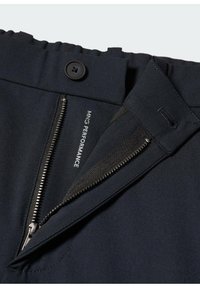Navy blue housut, joissa on vetoketjupääntie, nappisulku ja "MNG PERFORMANCE" -merkki. Sujuva kangas, jossa on istuva leikkaus.
