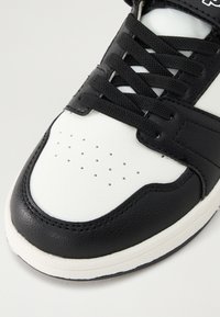 Sapatilha atlética em preto e branco com superior em couro texturizado, design de atacadores, perfurações para respirabilidade e sola em borracha.