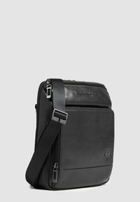 Borsa a spalla in pelle nera con una forma quadrata elegante. Presenta una chiusura con zip, una tracolla regolabile e dettagli testurizzati.