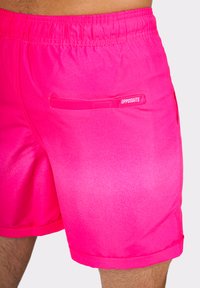 Vibrant pink short swim trunks featuring a smooth texture, elastic waistband, and a back pocket with flap. Clear "OPPOSUITS" branding detail.