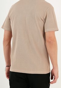 Kortärmad, beige ribbad t-shirt med strukturerad tyg, med rund halsringning och en avslappnad passform, sedd bakifrån.