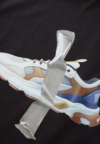 Sneaker-Grafik auf einem schwarzen Shirt, das ein weißes, blaues und beige Design mit Mesh-, Lederakzenten und silbernem Klebeband über dem Schuh zeigt.