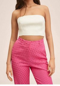Top corto sin mangas de color blanco hecho de una tela texturizada, combinado con pantalones rosa de cintura alta con lunares tonales y un acabado suave.