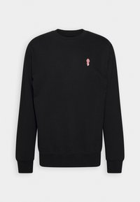 Sweat-shirt noir à manches longues et col rond avec petit emblème de torche rouge et blanc sur la poitrine gauche, présenté sur fond clair uni.