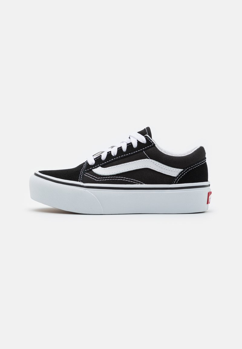 Zapatillas de lona negras con cordones blancos y una franja lateral blanca. Presentan una suela de goma blanca gruesa y una etiqueta de logo roja en el talón.