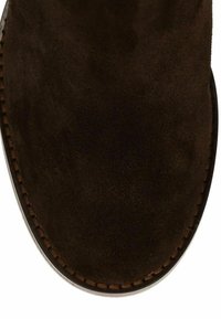 Bottine en daim marron avec un bout arrondi, une texture lisse et des surpiqûres contrastantes le long du bord de la semelle.