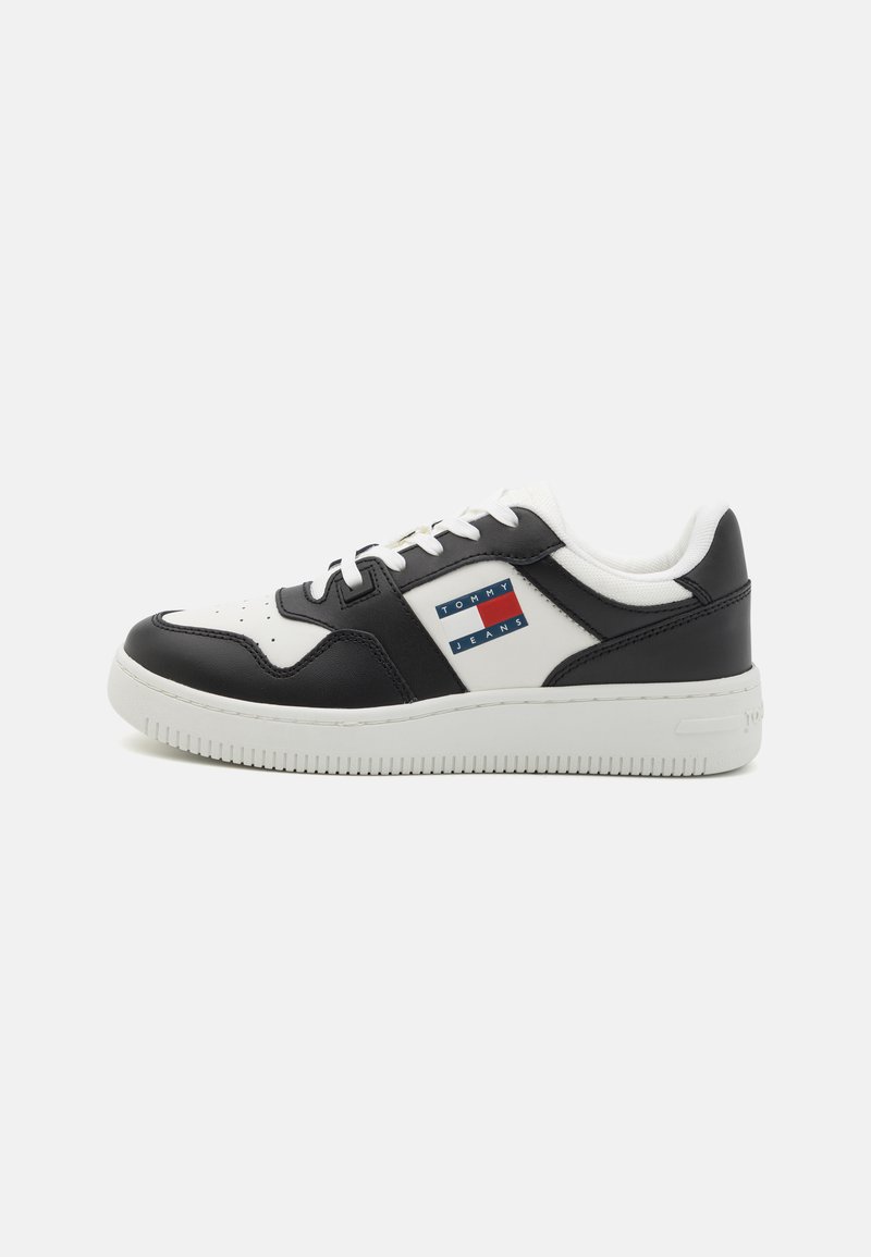 Svart og hvit lær sneakers med en teksturert såle, med et logopatch i rød, hvit og blå på yttersiden.