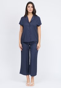 Top corto a maniche corte di colore blu navy con taschino sul petto abbinato a pantaloni larghi e morbidi. Realizzato in tessuto morbido con una vestibilità comoda.