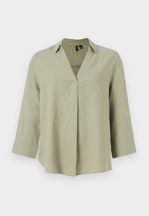 Olīvu zaļas lina krekls ar V formas kaklu, garām piedurknēm un atbrīvotu piegriezumu. Izceļas ar centrālo šuvuma detaļu un sarullētām piedurknēm.