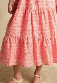 Ružová šaty s tiered strihom a kvetinovým vzorom, s volánovým lemom a ľahkou tkaninou. Sandále na popruhoch dopĺňajú outfit.