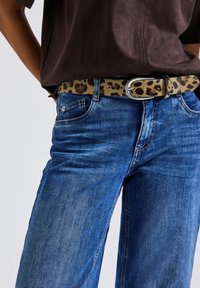 Blauwe denim jeans met een ontspannen pasvorm, geaccentueerd door een tan riem met een luipaardprint en een zilveren gesp. Bruin shirt met korte mouwen.