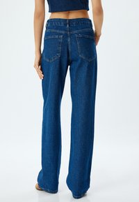 Leveled blue denim jeans with wide legs and a high waist, featuring visible back pockets and a raw hem. The fabric looks durable with a slight texture.