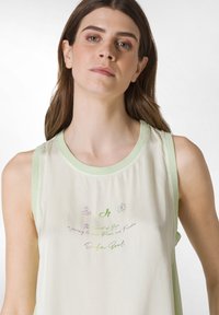 Lys beige tanktop med en mintgrøn halsudskæring og ærmegab. Har trykt tekst i farverig typografi og små grafikker.