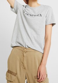 Grå bomulds t-shirt med et sort "København Danmark" logo, rund halsudskæring og afslappet pasform, parret med beige cargo bukser med lommer.