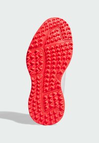 Red rubber shoe sole with a textured grip pattern, featuring varying heights and shapes for traction. Flat and rounded edges.