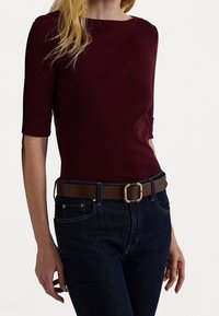 Burgunderfärgad topp med korta ärmar, parat med mörkblå jeans, surrad med ett brunt bälte med detaljer i guldspänne.