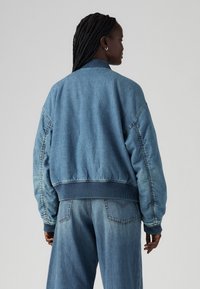 Jeans-Bomberjacke in Hellblau mit gerippten Bündchen und Saum, mit lockerem Schnitt und überschnittenen Schultern, von hinten gezeigt.