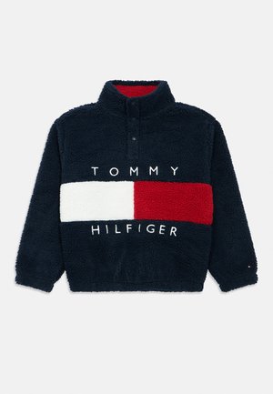 Marineblå fleecegenser med hvite og røde horisontale fargeblokker, halvlukket glidelåskrage og "Tommy Hilfiger"-tekst på fronten.