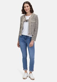 Tkany żakiet z tweedu w kolorze kremowym i czarnym z złotymi akcentami, w zestawie z białą koszulką z grafiką, niebieskimi dżinsami i białymi trampkami.