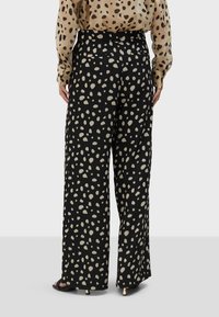 Čierne dlhé nohavice so širokým strihom a béžovým bodkovaným vzorom, s hladkou textúrou a pútkami na opasok. Sú viditeľné zadné vrecká.