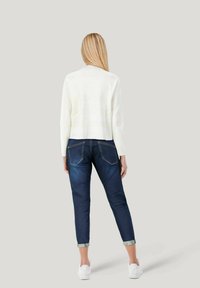 White, cropped sweater paired with dark blue jeans, featuring rolled cuffs and standard back pockets, complemented by white sneakers.