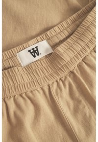 Pantaloni corti beige con cintura elasticizzata realizzati in un tessuto testurizzato, con un'etichetta bianca con scritte nere per l'identificazione del marchio.
