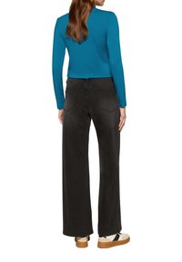 Langwerpige mouwloze aquamarijn top en hoge zwarte wijde jeans. De outfit heeft een soepele textuur en wordt gecombineerd met witte en bruine sneakers.