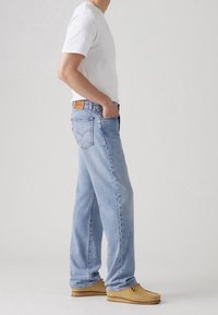 Jeans de mezclilla azul claro con un corte relajado, combinados con una camiseta blanca lisa y zapatos tipo mocasín de color marrón claro.