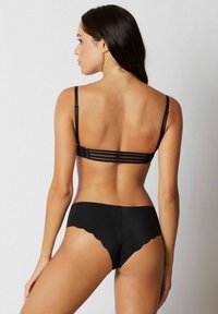 Set de lenjerie neagră, cu fund de margini ondulate și un sutien structurat, cu bretele reglabile și închidere la spate. Textură de țesătură netedă.