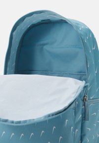 Ljusblå ryggsäck med ett mönster av små vita swooshes, dragkedjestängning och ett rymligt inre med en ljusfärgad foder.