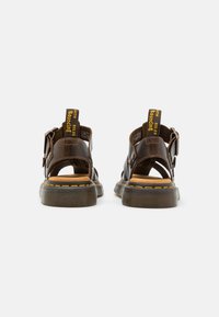 Ruske nahkasaappat avatud disainiga, reguleeritavate rihmadega, kollaste detailidega kanna lingil ja õmblustes ning tekstureeritud tallaga.