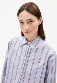 Lichtpaarse geknoopte blouse met verticale strepen in oranje en marineblauw. Heeft een puntige kraag en een borstzak. Glad stoftextuur.