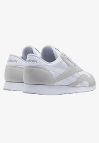 Vita och ljusgrå sneakers i läder och mocka, med snörning, logodetaljer och en texturerad gummisula.