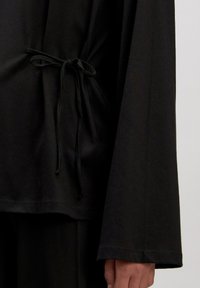 Zwarte lange mouwen top van zachte stof, met een cinched taille met een strik en brede mouwen. Glad textuur en minimalistisch ontwerp.