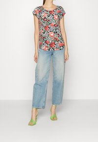 Top de manga corta con patrón floral en negro, rojo y verde, combinado con unos jeans rectos de tiro claro y tacones verdes con tiras.