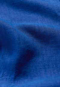 Tessuto blu con una texture liscia, caratterizzato da un aspetto leggermente stropicciato e un motivo intrecciato, che riflette la luce in diverse tonalità.