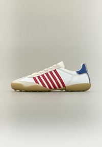 Λευκό αθλητικό παπούτσι με κόκκινες ρίγες, μπλε λεπτομέρεια στη φτέρνα, μπεζ σόλα και μπεζ κορδόνια, σε πλάγια όψη σε ουδέτερο φόντο.