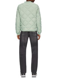  Lichtgroene gewatteerde jas met een ronde halslijn, ribbelmanchetten en minimale stikseldetails, gecombineerd met donkergrijze jeans en sneakers.