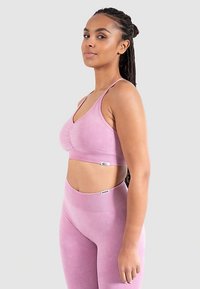 Vaaleanpunainen urheilurintaliivit ja siihen sopivat korkeavyötäröiset leggingsit, joissa on sileä pinta ja hillitty design sekä logo vyötärönauhassa.