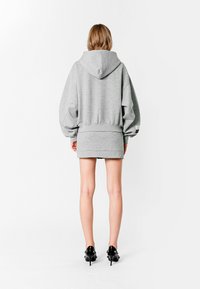 Sudadera gris de gran tamaño con capucha ajustable, puños y dobladillo acanalados, combinada con una minifalda gris. Textura de tela suave; zapatos negros.