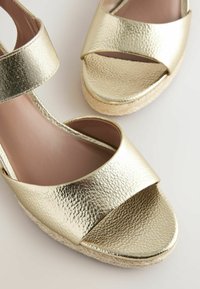Sandali espadrilles dorati con una finitura metallica strutturata, punta aperta e una fascia larga. Suola in rafia intrecciata resistente per un maggiore comfort e altezza.