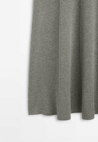 Rideau en tissu tricoté gris doux suspendu avec des coutures verticales subtiles et des plis délicats sur fond blanc.